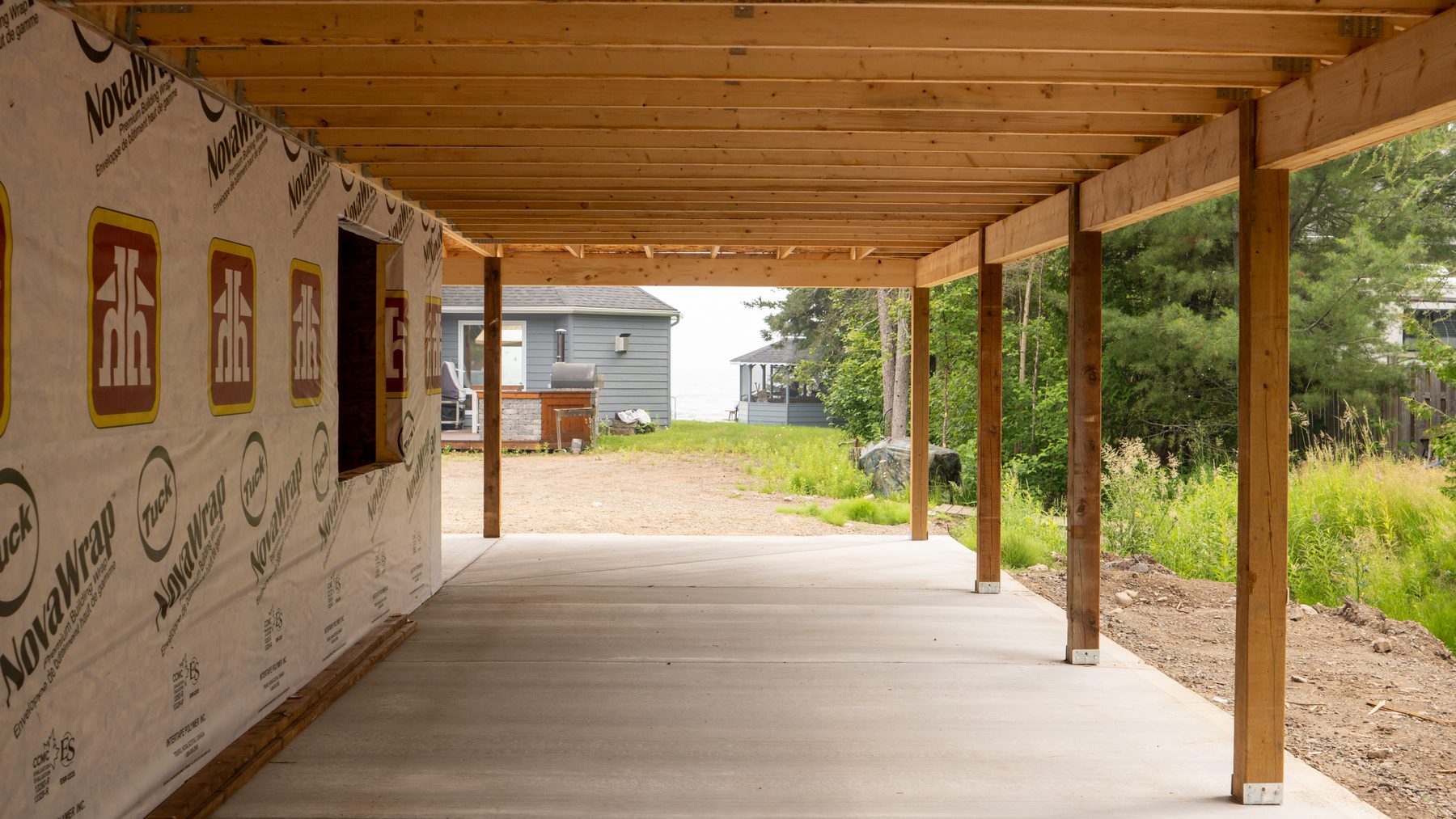 Framed covered walkway with house wrap looking out toward a lakeside cottage and water