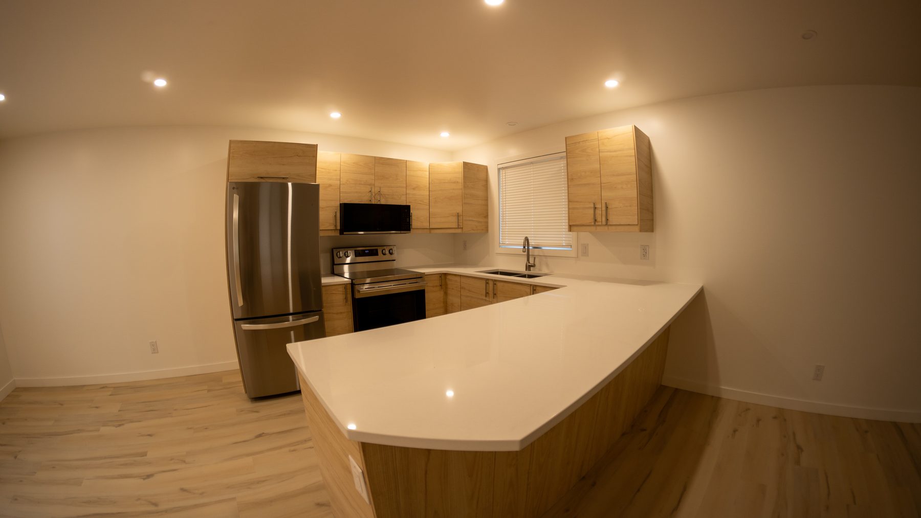 Finished kitchen with light wood cabinetry, stainless appliances and a white quartz peninsula counter