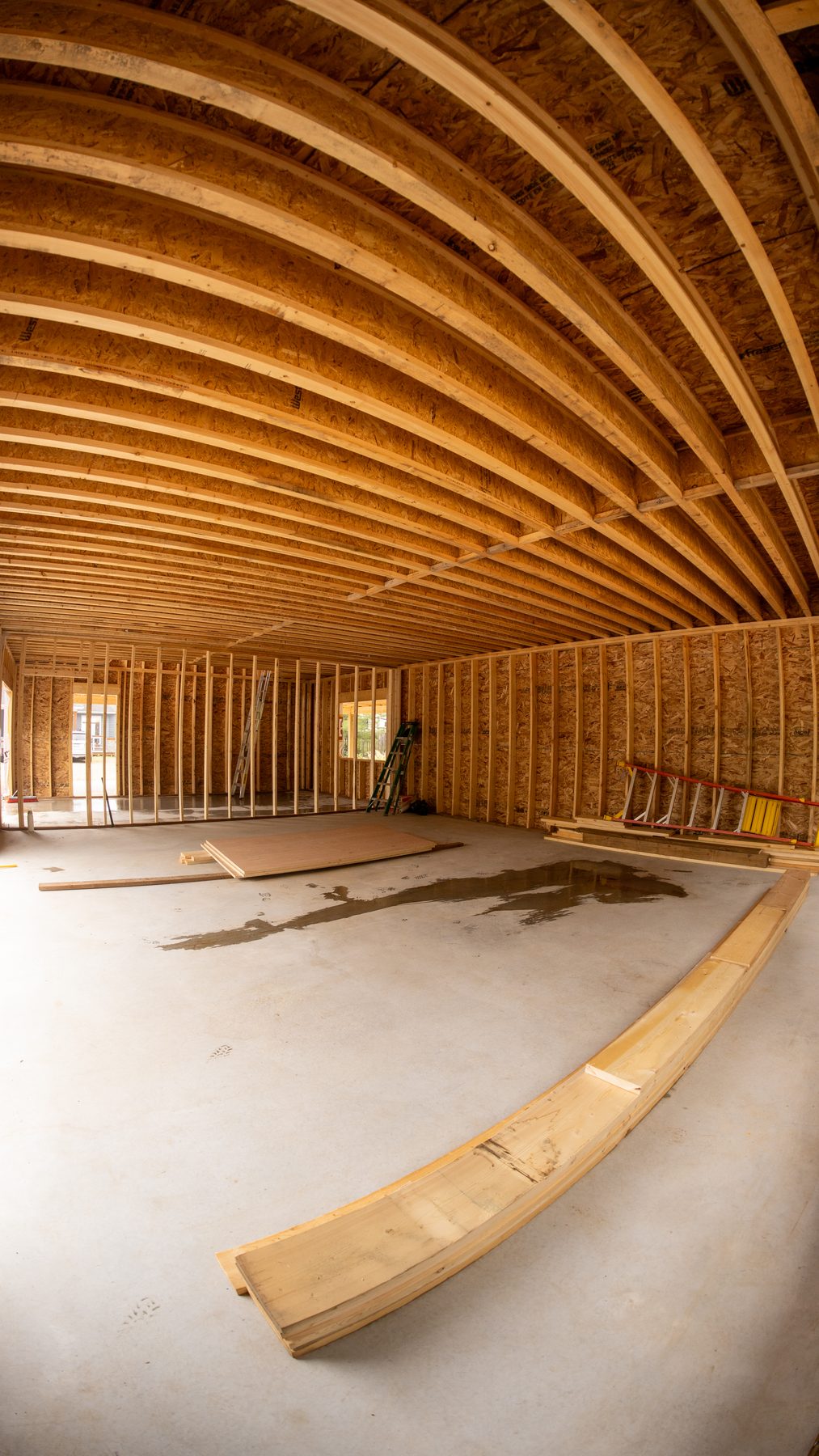Interior of a new-construction great room with curved laminated roof beams and open stud walls